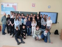 Na tle zielonej tablicy szkolnej znaduje się grupa wszystkich uczestników konkursu, po lewej nauczyciel chemii, a po prawej- nauczycielka fizyki. Wszyscy są uśmiechnięci i w dobrych humorach.