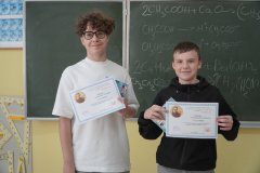 W sali lekcyjnej na tle zielonej tablicy szkolnej znajduje się dwóch uczestników konkursu- zdobywców 1 miejsca w konkursie. Uczniowie trzymają w rękach tematyczne dyplomy i nagrody książkowe.