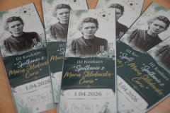 Na ławce szkolnej znajduje się kilka własnoręcznie wykonanych zakładek do książek- upominków dla każdego uczestnika konkursu. Na zakładce znajduje sie wizerunek Marii Skłodowskiej- Curie oraz napisy: "III Konkurs Spotkanie z Marią Skłodowską- Curie 1.04.2026".