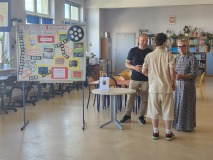 Pani dyrektor wręcza nagrodę dziecku. Obok tablica z wydrukowanymi pracami z konkursu multimedialnego. W tle biblioteka.