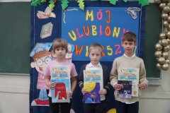 Zdjęcie przedstawia trzech Laureatów konkursu w kategorii uczniów klas pierwszych. Dzieci stoją na tle dekoracji, trzymając w rękach dyplomy i nagrody- książki.