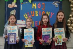 Zdjęcie przedstawia cztery Laureatki konkursu w kategorii uczniów klas drugich i trzecich. Dziewczynki stoją na tle dekoracji, trzymając w rękach dyplomy i nagrody- książki.