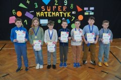 Siedmioro uczniów stoi na parkiecie sali gimnastycznej. Trzymają dyplomy, a na szyjach mają zawieszone medale za zajęcie pierwszego, drugiego i trzeciego miejsca w konkursie matematycznym.
