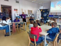 uczniowie siedzą przy stołach, słuchają prowadzącego nauczyciela, który pokazuje na plakat przedstawiający symbol wyprawy Sławosza