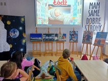 uczniowie siedzą przy stołach, leżą na dywanikach i oglądają film o polskim astronaucie