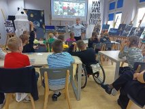 grupa uczniów z uwagą słucha prelekcji nauczyciela, w tle zdjęcie Sławosza Uznańskiego-Wiśniewskiego ze stacji kosmicznej