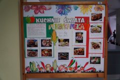 Na zdjęciu znajduje się kolorowa tablica zatytułowana „Kuchnie Świata – kuchnia meksykańska”. Widoczne są zdjęcia i opisy potraw, takich jak tacos, burritos, quesadilla czy nachos. Tablicę ozdabiają ilustracje papryczek chili, kukurydzy oraz innych warzyw. Utrzymana jest ona w żywych kolorach nawiązujących do flagi Meksyku.
