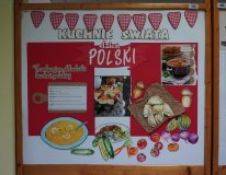 Tablica dekoracyjna zatytułowana „Kuchnie Świata – dzień polski”. Na środku widoczne są zdjęcia polskich potraw, między innymi pierogów i kapuśniaku. Po lewej stronie znajduje się lista tradycyjnych składników kuchni polskiej oraz rysunek talerza z zupą. Dookoła rozmieszczone są kolorowe ilustracje warzyw, takich jak buraki, pomidory, cebule i ogórki. Dekorację u góry tworzy girlanda z biało-czerwonych trójkątów.
