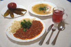Na stole stoi typowe danie kuchni włoskiej - spaghetti oraz pyszny kompot,  zupa, ogórki kiszone oraz jabłko.