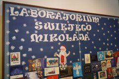 Tablica z granatowym tłem i białymi gwiazdkami, biały napis 'Laboratorium świętego Mikołaja", wokół mnóstwo kartek świątecznych.