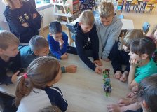 uczniowie zgromadzeni przy stole prezentują całej klasie skończony projekt z klocków LEGO