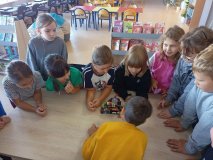 uczniowie zgromadzeni przy stole prezentują całej klasie skończony projekt z klocków LEGO