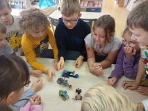 uczniowie zgromadzeni przy stole prezentują całej klasie skończony projekt z klocków LEGO