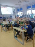 uczniowie przy stołach zgromadzeni w czytelni biblioteki i układający swoje projekty z klocków LEGO