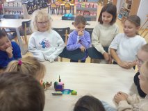 uczniowie zgromadzeni przy stole prezentują całej klasie skończony projekt z klocków LEGO