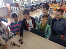 uczniowie przy stołach zgromadzeni w czytelni biblioteki i układający swoje projekty z klocków LEGO