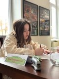 uczennica siedzi przy stole z długopisem w ręku, skupiona próbuje rozwiązać zadanie