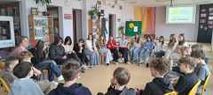 Uczniowie siedzący w kręgu uczestnicą w zajęciach.