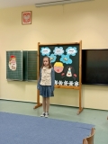 Na tle dekoracji dziewczynka recytuje przygotowany przez siebie utwór literacki.