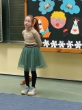 Na tle dekoracji dziewczynka recytuje przygotowany przez siebie utwór literacki.