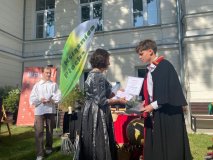 Wicedyrektor Książnicy Płockiej wręcza pamiątkowy dyplom dla szkoły uczniowi ubranemu w czarny surdut z epoki.