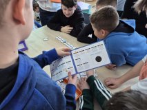 sześcioro uczniów zgromadzonych wokół stołu układa z drewnianych puzzli trasy dla ozobotów.