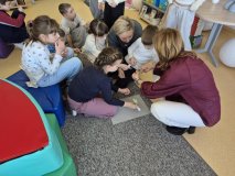 grupa uczniów z nauczycielami bierze udział w zabawie czytelniczej – składa i przykleja na kolorowe kartki rozsypane tytuły książek.