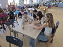 uczennice siedzą przy stole w czytelni i próbują wykonać zadanie – ułożyć pomieszane fragmenty tytułów.