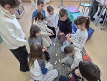 uczniowie siedząc na dywaniku próbują wykonać zadanie – ułożyć pomieszane fragmenty tytułów.