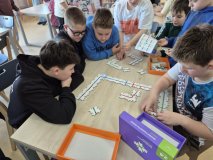 grupa uczniów pochyla się nad stołem, po rozłożonych puzzlach jeżdżą ozoboty.