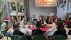 Na tle zimowo-świątecznej dekoracji grupa uczniów siedzi wokół pięknie udekorowanego stołu.