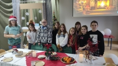 Na tle zimowo-świątecznej dekoracji, wokół pięknie udekorowanego grupa uczniów pozuje do zdjęcia.