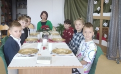 Na tle zimowo-świątecznej dekoracji sześciu chłopców wraz z nauczycielką siedzi wokół pięknie udekorowanego stołu.