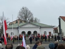 Uroczystości Obchodów Narodowego Święta Niepodległości przed Płytą Nieznanego Żołnierza w Płocku. Na podium stoją żołnierze, harcerze i przedstawiciele władz, a za nimi widać liczne poczty sztandarowe z biało-czerwonymi flagami. W pierwszym planie zgromadzeni uczestnicy obserwują ceremonię 