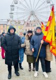 Chłopiec- uczeń SP nr 22 w Płocku, trzymający w ręku flagę Orszaku Trzech Króli -  stoi w towarzystwie mamy, babci i starszego brata na Starym Rynku; w tle koło widokowe oraz kamienica.