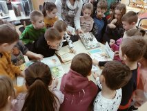 Grupa dzieci wokół stołu z zaciekawieniem ogląda wyłożone na stole „Książki niechciane” – zniszczone, poplamione, porwane.