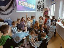 Grupa pierwszaków stoi wokół niezwykłej książki rozkładanej jak mapa. 