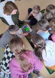 Uczniowie skupiają się wokół telefonu, którym bibliotekarka skanuje książkę z rozszerzona rzeczywistością i na ekranie telefonu pierwszoklasiści obserwują dodatkowe ilustracje w formacie 3d.