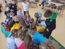 Grupa uczniów siedząca na dywanie skupiona wokół interesującej leżącej na podłodze książki.