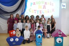 Zdjęcie grupowe klasy 1a, uczniowie pozują w kolorowych strojach, wokół nich figury zabawnych potworków.