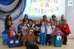 Zdjęcie grupowe klasy 1d, uczniowie pozują w kolorowych bajkowych strojach, wokół nich figury zabawnych potworków.