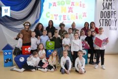 Zdjęcie grupowe klasy 1f, uczniowie pozują w galowych strojach, wokół nich figury zabawnych potworków.
