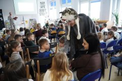 Pierwszoklasiści odpowiadają do mikrofonu ucznia w przebraniu wilka na zagadki związane z biblioteką i bajkami. 