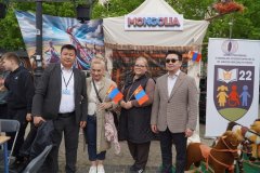 Cztery osoby stoją przed stoiskiem Mongolii, a dwie z nich trzymają mongolskie flagi.