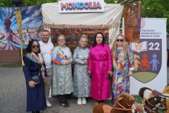 Grupa osób stoi przed stoiskiem Mongolii, a na pierwszym planie widoczne są drewniane zabawkowe koniki.