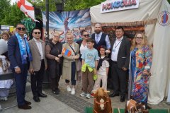 Dorośli i dwoje dzieci stoją przed namiotem oznaczonym napisem „MONGOLIA”, a na pierwszym planie znajdują się drewniane zabawkowe konie.