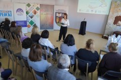 rozpoczęcie konkursu, pomieszczenie biblioteki, kobieta – bibliotekarka stoi na środku i  wita w imieniu gospodarzy przybyłych gości