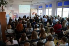 biblioteka szkolna, widok ogólny na siedzącą na krzesłach widownię, w tle przemawia pani Dyrektor szkoły