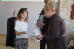 Dyrektor Szkoły Podstawowej nr 22 i przewodnicząca jury wręczają dziewczynce dyplom i torbę z logo konkursu