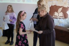 Dyrektor Szkoły Podstawowej nr 22 i przewodnicząca jury wręczają dziewczynce dyplom i torbę z logo konkursu, w tle stoi z dyplomem inna laureatka